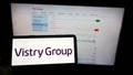 Person holding mobile phone with logo of British housebuilding company Vistry Group plc on screen in front of web page.