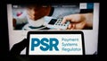 Person holding mobile phone with logo of British Payment Systems Regulator (PSR) on screen in front of web page. Royalty Free Stock Photo