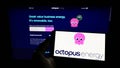 Person holding mobile phone with logo of British renewables company Octopus Energy Group on screen in front of web page.