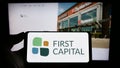 Person holding mobile phone with logo of Canadian real estate company First Capital REIT on screen in front of web page.