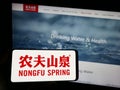 Person holding mobile phone with logo of Chinese business Nongfu Spring Company Limited on screen in front of web page.