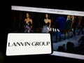 Person holding mobile phone with logo of Chinese fashion company Lanvin Group on screen in front of business web page.
