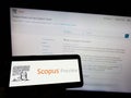 Person holding mobile phone with logo of citation database Scopus Preview on screen in front of business web page.