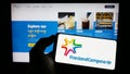 Person holding mobile phone with logo of company Koninklijke FrieslandCampina NV on screen in front of business web page.