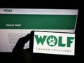 Person holding mobile phone with logo of company Wolf Carbon Solutions on screen in front of business web page.