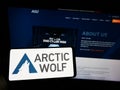 Person holding mobile phone with logo of cybersecurity company Arctic Wolf Networks Inc. on screen in front of web page.