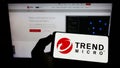 Person holding mobile phone with logo of cybersecurity company Trend Micro Inc. on screen in front of business web page. Royalty Free Stock Photo