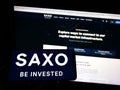 Person holding mobile phone with logo of Danish investment banking company Saxo Bank AS on screen in front of web page. Royalty Free Stock Photo