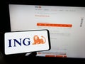 Person holding mobile phone with logo of Dutch financial services company ING Groep NV on screen in front of web page.