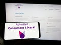 Person holding mobile phone with logo of Dutch regulator Autoriteit Consument en Markt (ACM) on screen with web page.