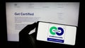 Person holding mobile phone with logo of environmental label Cradle to Cradle Certified on screen in front of web page.