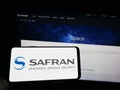 Person holding mobile phone with logo of French aerospace company Safran SA on screen in front of business web page. Royalty Free Stock Photo