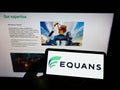 Person holding mobile phone with logo of French facility management company EQUANS on screen in front of business web page.