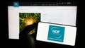 Person holding mobile phone with logo of French hydrogen company HDF Energy on screen in front of business web page.