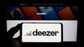 Person holding mobile phone with logo of French music streaming company Deezer SA on screen in front of business web page.