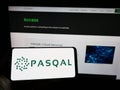 Person holding mobile phone with logo of French quantum processing company PASQAL SAS on screen in front of web page.