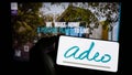 Person holding mobile phone with logo of French retail company Adeo SA on screen in front of business web page.