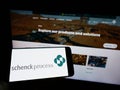 Person holding mobile phone with logo of German company Schenck Process Europe GmbH on screen in front of web page. Royalty Free Stock Photo