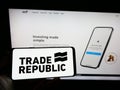 Person holding mobile phone with logo of German company Trade Republic Bank GmbH on screen in front of business web page.