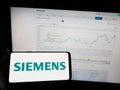 Person holding mobile phone with logo of German conglomerate Siemens AG on screen in front of business web page.