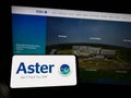 Person holding mobile phone with logo of health company Aster DM Healthcare Limited on screen in front of web page.
