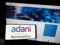 Person holding mobile phone with logo of Indian company Adani Green Energy Limited on screen in front of web page.