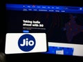 Person holding mobile phone with logo of Indian telecommunications company Reliance Jio on screen in front of web page.