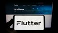 Person holding mobile phone with logo of Irish bookmaking company Flutter Entertainment plc on screen in front of web page. Royalty Free Stock Photo