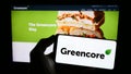 Person holding mobile phone with logo of Irish food company Greencore Group plc on screen in front of business web page.