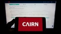 Person holding mobile phone with logo of Irish housebuilding company Cairn Homes plc on screen in front of web page.