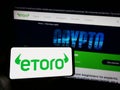 Person holding mobile phone with logo of Israeli social trading company eToro on screen in front of business web page.