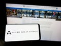 Person holding mobile phone with logo of issuer Reserve Bank of Australia (RBA) on screen in front of web page.