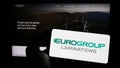 Person holding mobile phone with logo of Italian company EuroGroup Laminations S.p.A. on screen in front of web page.