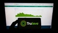 Person holding mobile phone with logo of medical marijuana company Trulieve Cannabis Corp. on screen in front of web page.