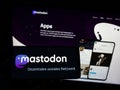 Person holding mobile phone with logo of open-source social media software Mastodon on screen in front of web page.