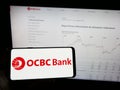 Person holding mobile phone with logo of Oversea-Chinese Banking Corporation (OCBC Bank) on screen in front of web page. Royalty Free Stock Photo