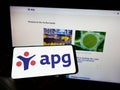 Person holding mobile phone with logo of pension fund Algemene Pensioen Groep (APG) on screen in front of web page.