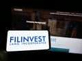 Person holding mobile phone with logo of real estate company Filinvest Land Inc. (FLI) on screen in front of web page.