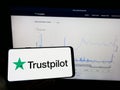 Person holding mobile phone with logo of review platform company Trustpilot Group plc on screen in front of web page.