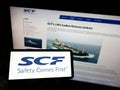 Person holding mobile phone with logo of Russian shipping company Sovcomflot (SCF) on screen in front of webpage. Royalty Free Stock Photo