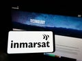 Person holding mobile phone with logo of satellite company Inmarsat Global Limited on screen in front of business web page. Royalty Free Stock Photo