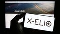 Person holding mobile phone with logo of Spanish renewables company X-ELIO Energy S.L. on screen in front of web page.