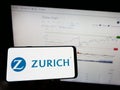 Person holding mobile phone with logo of Swiss financial company Zurich Insurance Group AG on screen in front of web page.