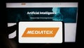 Person holding mobile phone with logo of Taiwanese semiconductor company MediaTek Inc. on screen in front of web page.