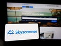 Person holding mobile phone with logo of travel metasearch company Skyscanner Ltd. on screen in front of web page.