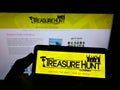 Person holding mobile phone with logo of The Treasure Hunt Company (Brighton) on screen in front of business web page.