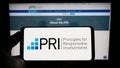 Person holding mobile phone with logo of UN Principles for Responsible Investment (PRI) on screen in front of web page.