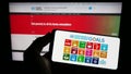 Person holding mobile phone with logo of UN Sustainable Development Goals (SDG) on screen in front of web page.