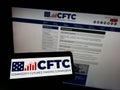 Person holding mobile phone with logo of US Commodity Futures Trading Commission (CFTC) on screen in front of web page.