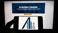 Person holding mobile phone with logo of US consulting company Alvarez and Marsal LLC on screen in front of web page.